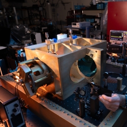 A photo of an interferometer on a lab bench. A staff member is adjusting a part of it.