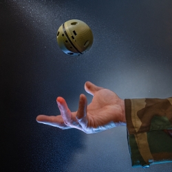 A 3D-printed baseball-sized sphere is thrown in the air by a person offscreen wearing a camo jacket. 