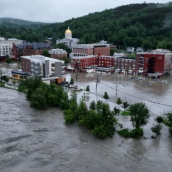 An image showing the flooded streets of Montpelier. Flood water surround brick buildings and roads. 