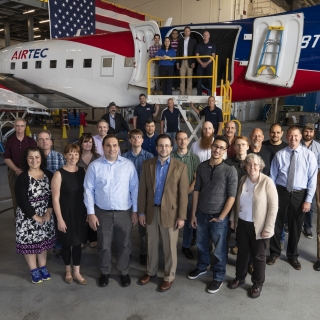 A group of about 30 people pose in front of an airplane