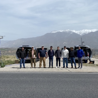 A team of eight stands in front of two sensor-equipped vehicles, with mountains in the backdrop. 