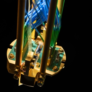 An up-close of a quantum repeater module mounted on a gold-plated copper assembly and connected to green printed circuit boards, with optical fibers routed up.