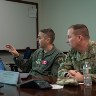 Colonel Joseph Monaco, left, and Lieutenant Colonel Tim Heaton sit at a table discussing a presentation they are being briefed on.
