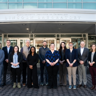 A group photo of PMI and MIT LL team outside of the main Lincoln Laboratory entrance.