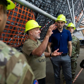 Jeffrey Dominick leads students on a tour of the Millstone Hill Radar. They wear yellow hardhats and listen attentively to Dominick's explanation as he gestures. 
