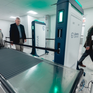 Two individuals walk past a security screening system. 