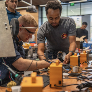 Two SOCOM participants sit at a table full of hardware components. 