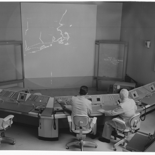 Two operators sit in front of a digital display showing an air defense network.