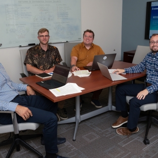 Four researchers sit around a conference table, smiling for a photo. 