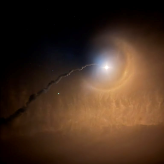Photo of the H-3 launch vehicle, dark background with a launch trajectory ending in a bright point of light. 