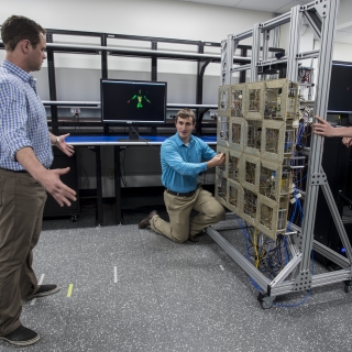 Researchers test the prototype standoff microwave imaging system. The antennas emit radio signals that reflect off the person standing in front of the array; the system processes the reflections to create the image on the monitors in the background.