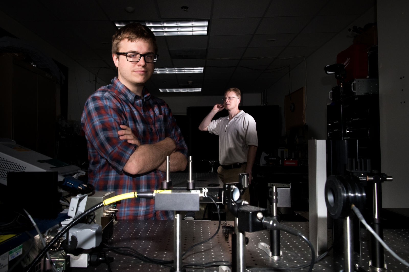 Two men standing in a laboratory with a laser transmitter setup 