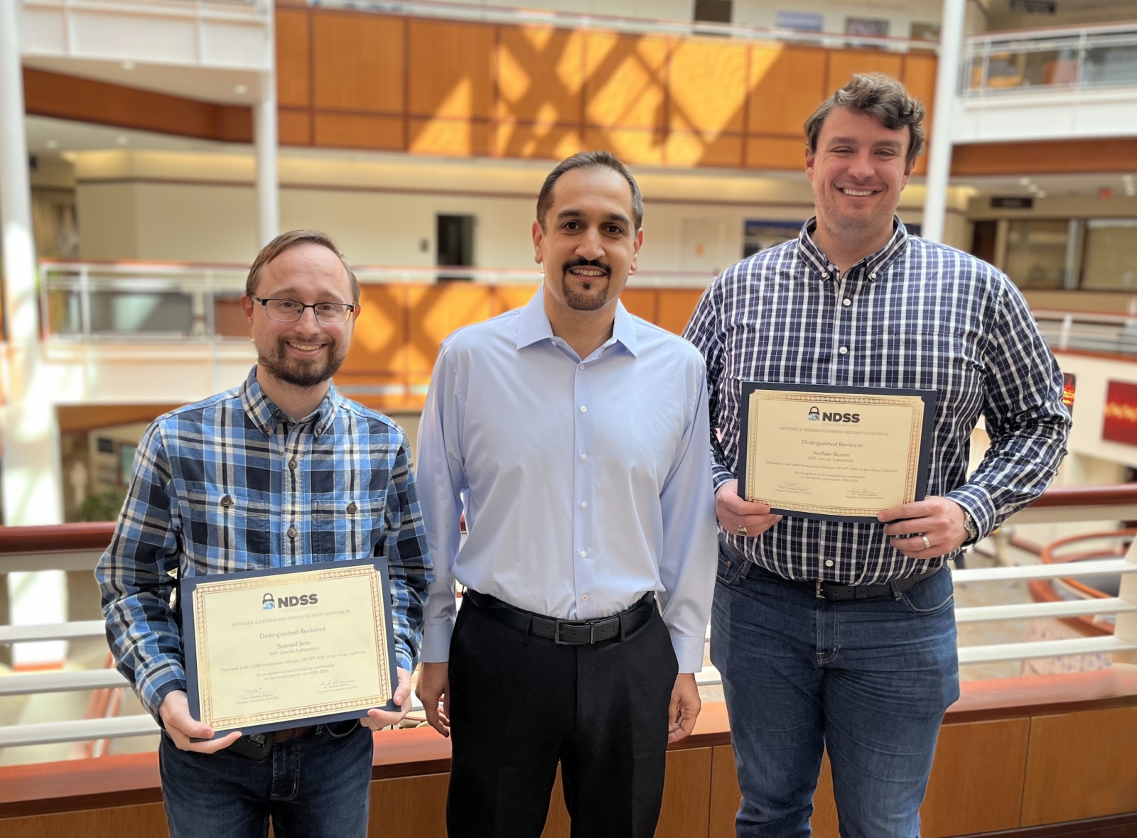 Three staff members pose for a group photo in a sunny atrium.