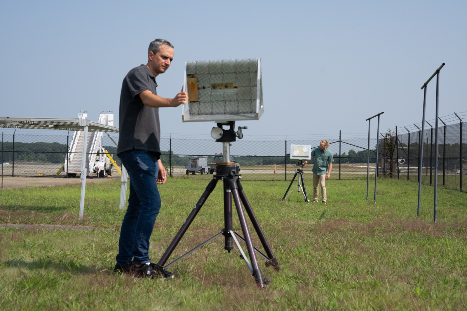Two individuals inspect two radar and communications systems outdoors. 