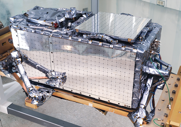 A closeup of one of the Laboratory-built payloads. The payload is silver in color and rectangular box-shaped with a few protrusions on the sides. 