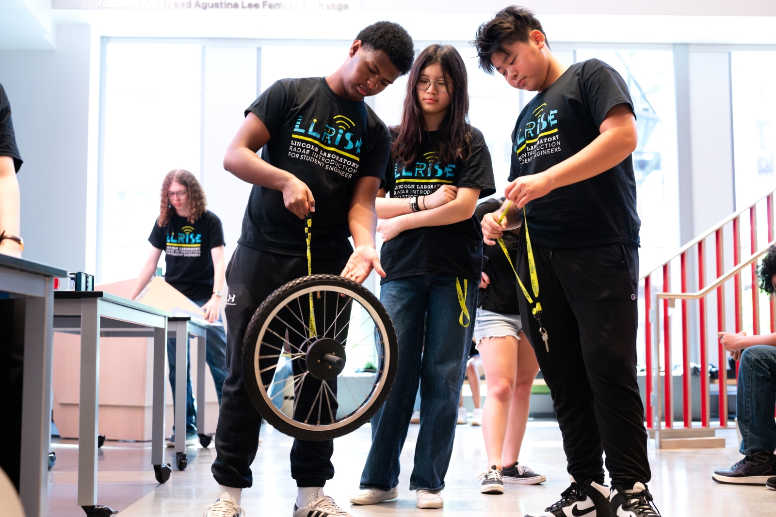 Three LLRISE students are together with one holding a wheel that is hanging from a yellow lanyard. 