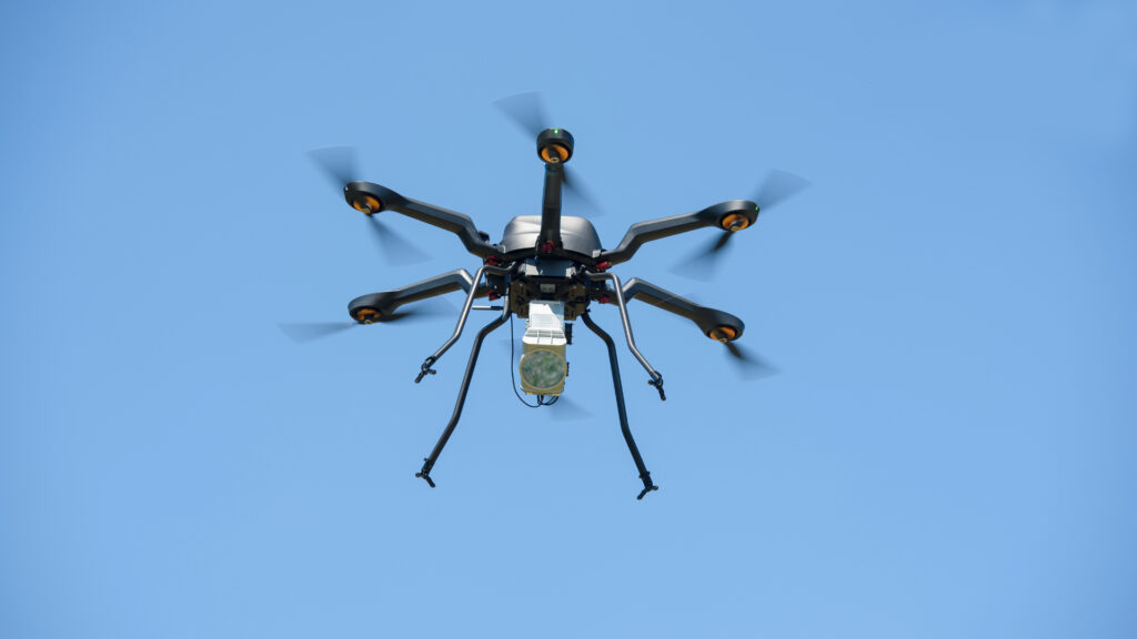 A small drone flying against a blue-sky background