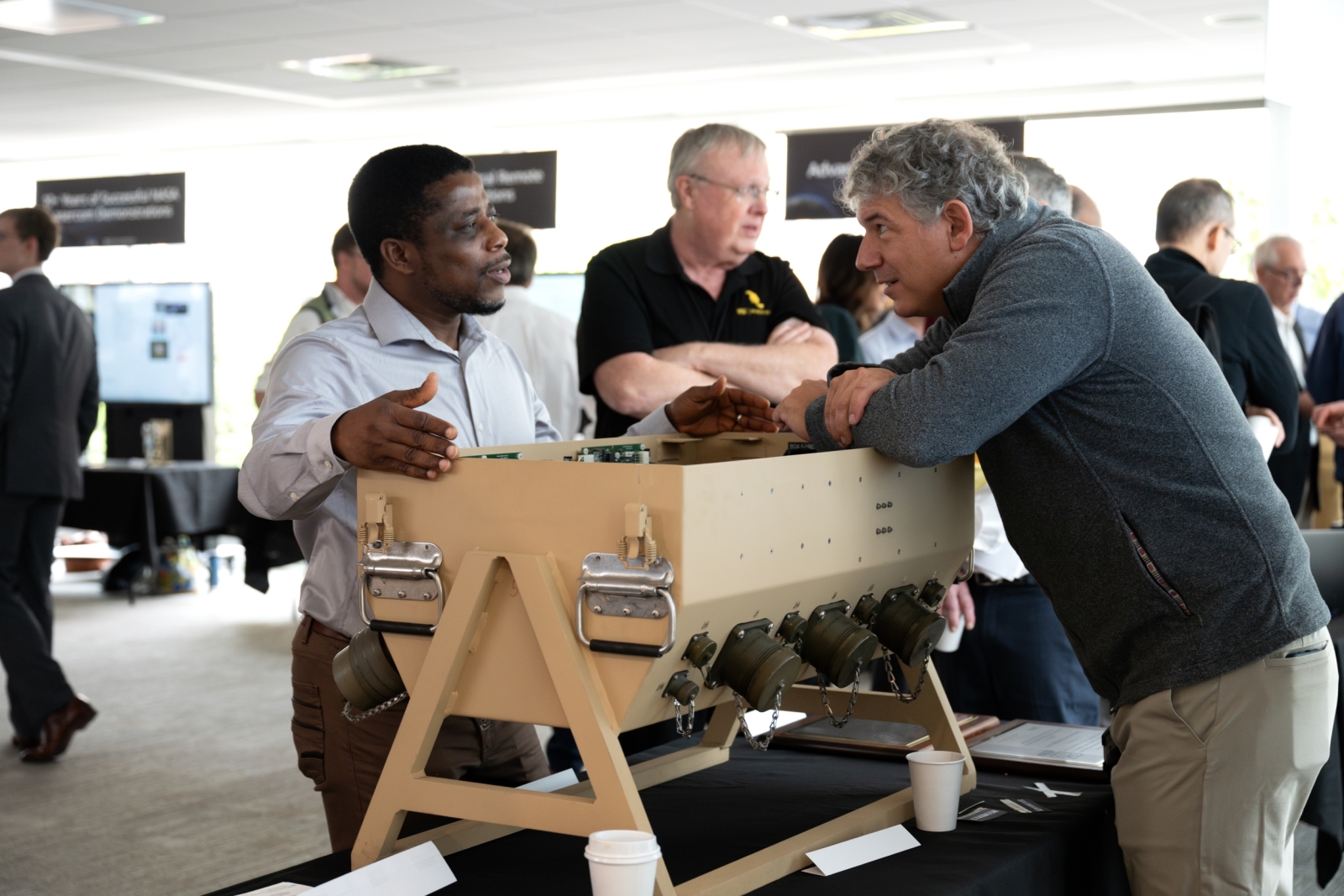 An expo attendee chats with a staff member about a technology that is a large pale brown box resting an an exhibition table.