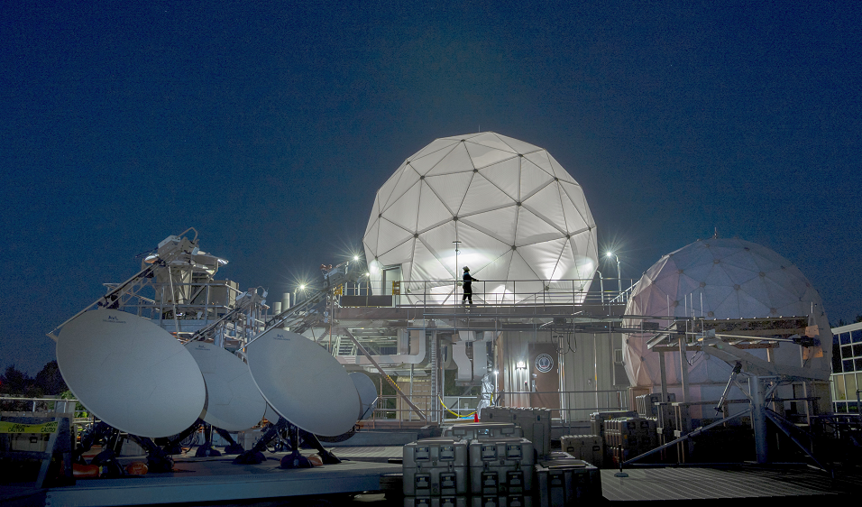 Four satellite dishes and two radomes, each covering satellite communications antennas, are shown on the roof of Lincoln Laboratory among other equipment.