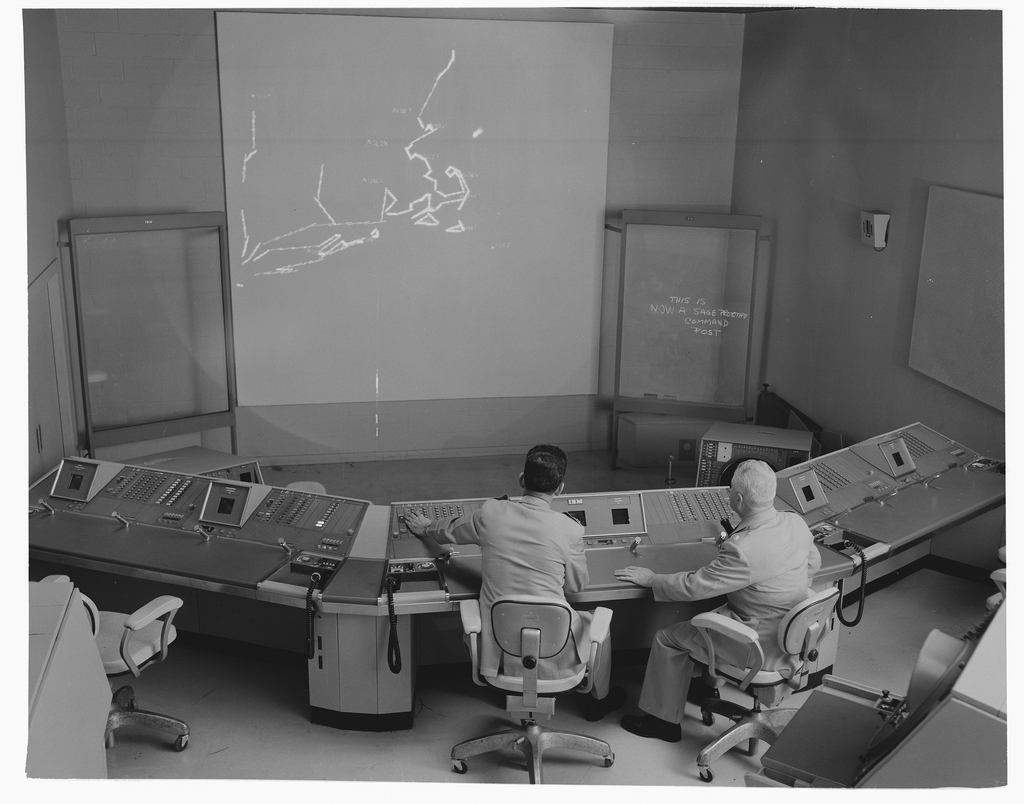 Two operators sit in front of a digital display showing an air defense network.