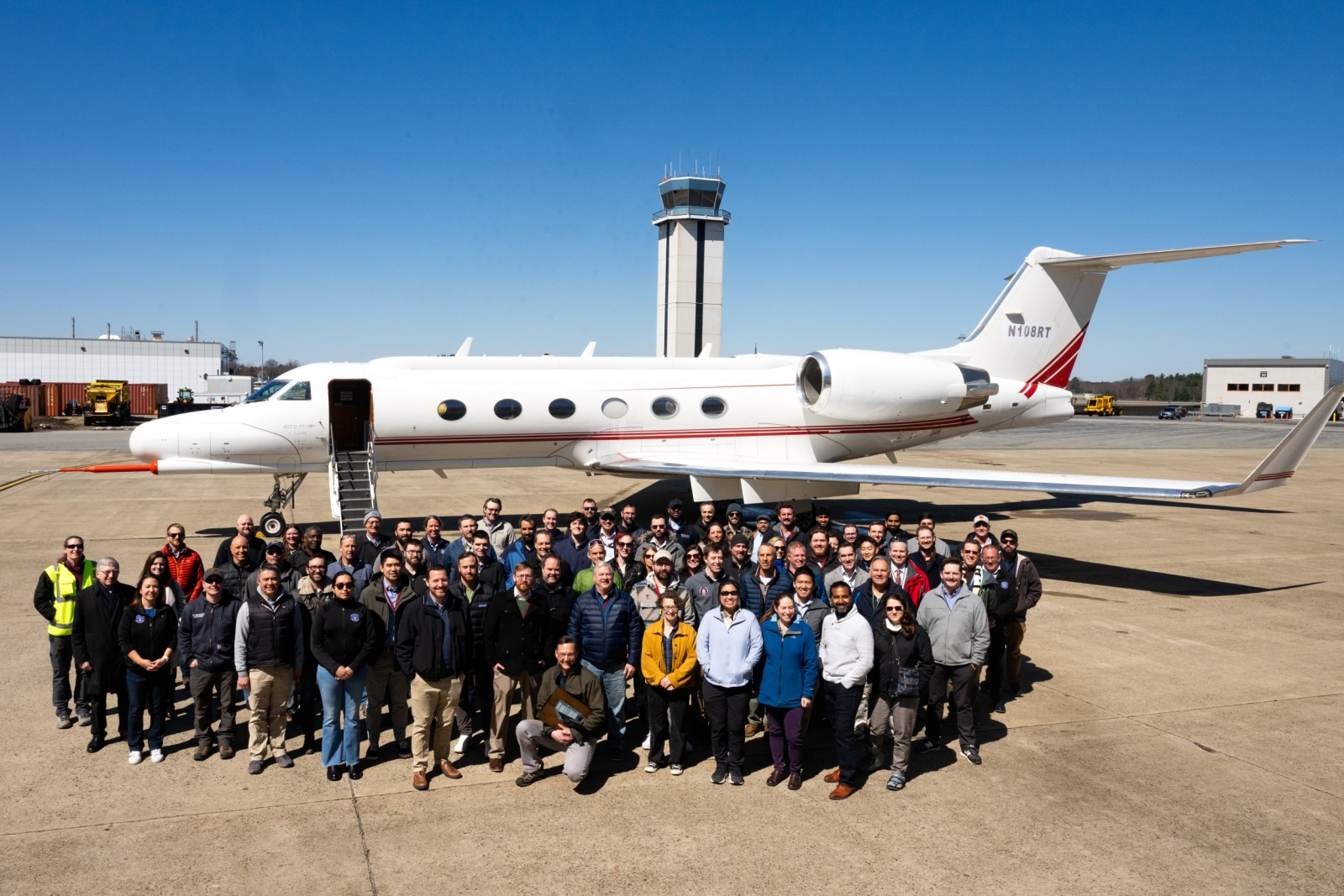 A large group gathers outside in front of an aircraft.