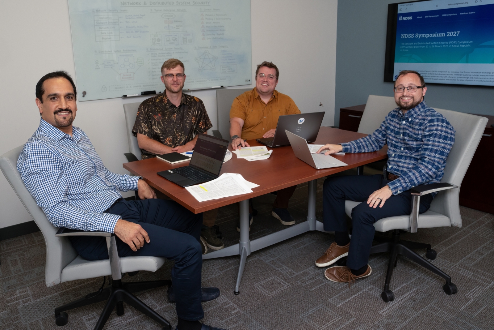 Four researchers sit around a conference table, smiling for a photo. 