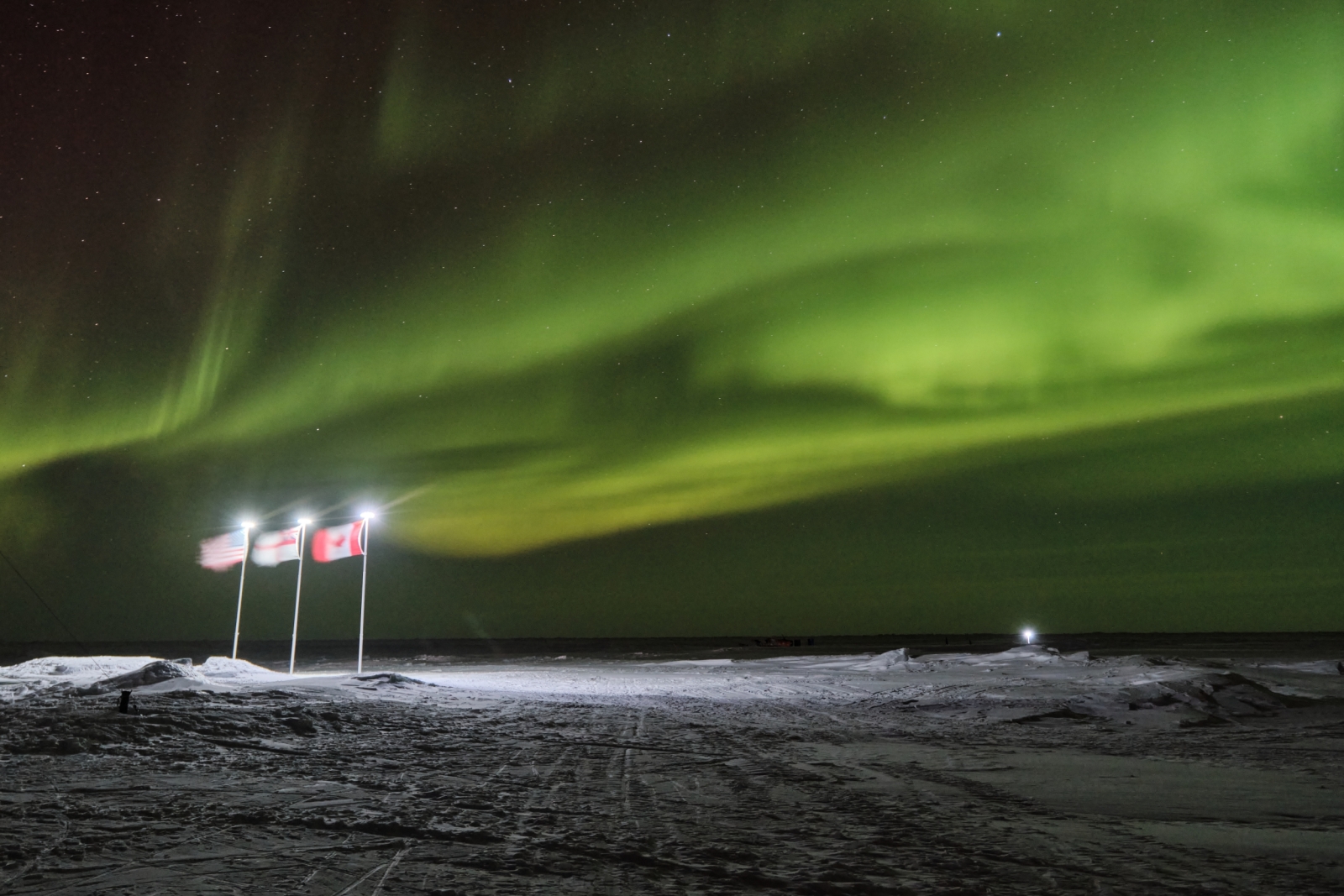 Three flags are planted in the Arctic ice against a backdrop of the northern lights.