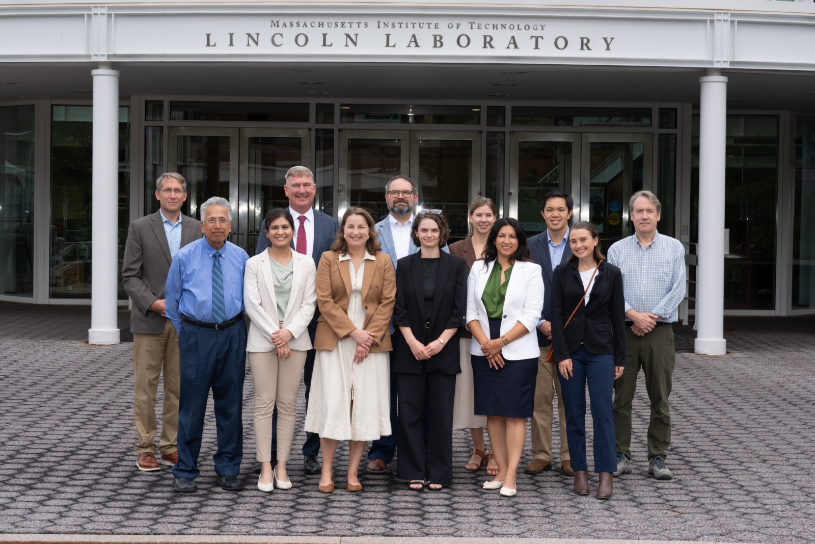 A group of 12 individuals standing in front of lincoln laboratory entrance. 