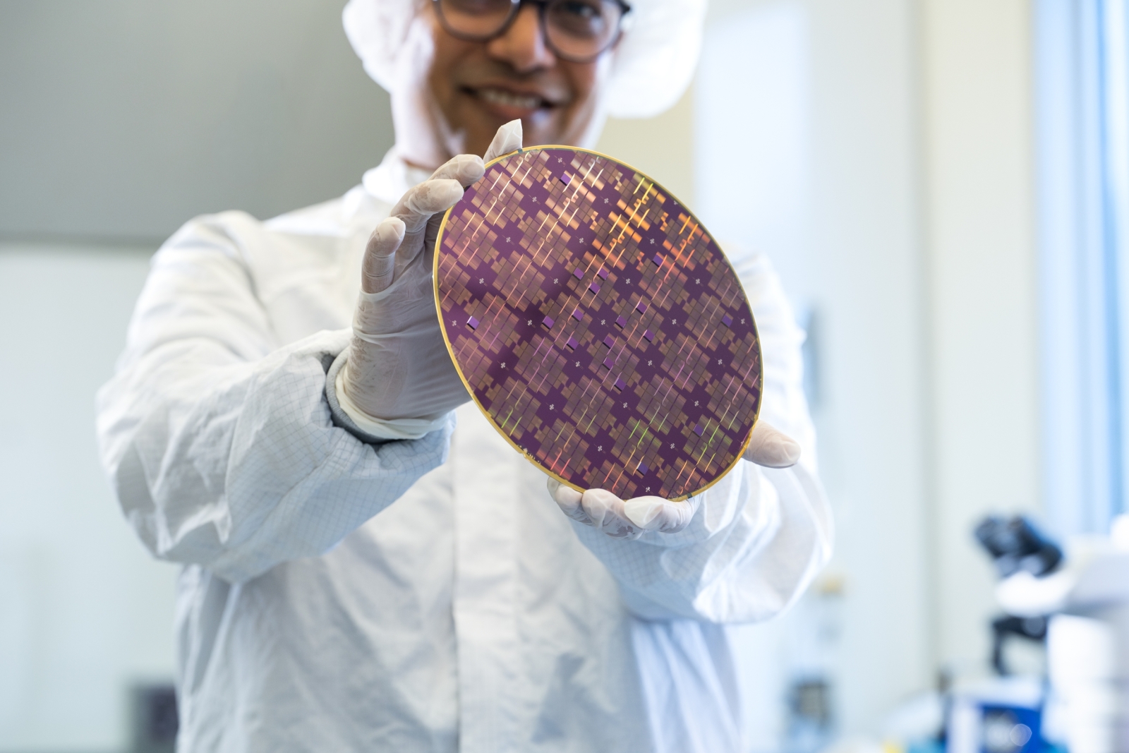 Rabindra Das (wearing microelectronics protective clothing within a fabrication space), holds an 8-inch wafer containing integrated circuits. 