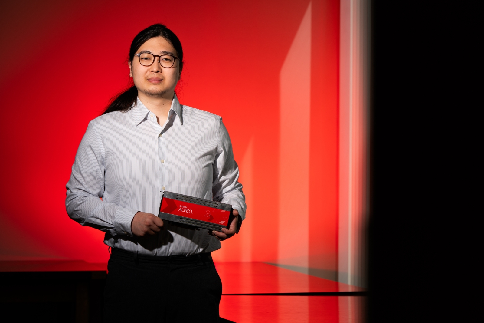 A photo of Jeffery Lim against a red background, holding a hardware platform (rectangle, about 4 by 12 inches). 