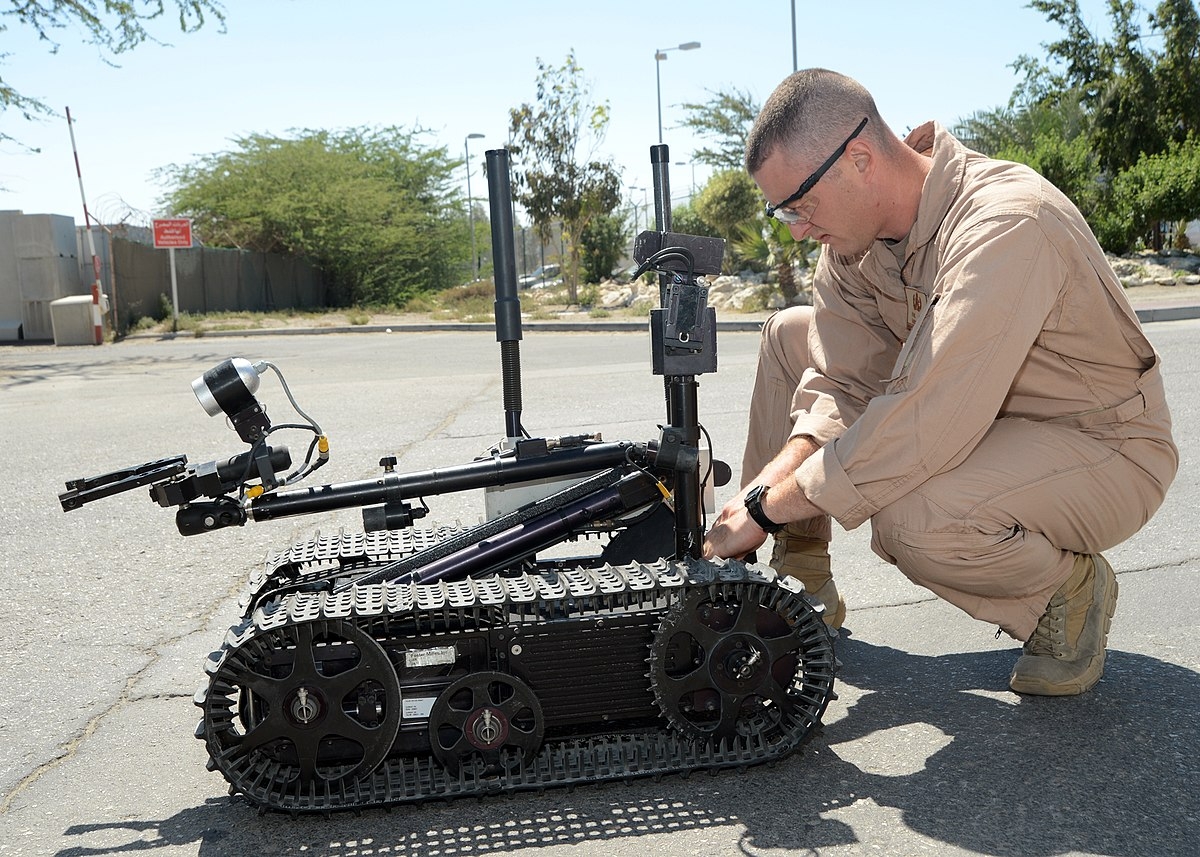 A photo of a service member preparing a small autonomous robot. 