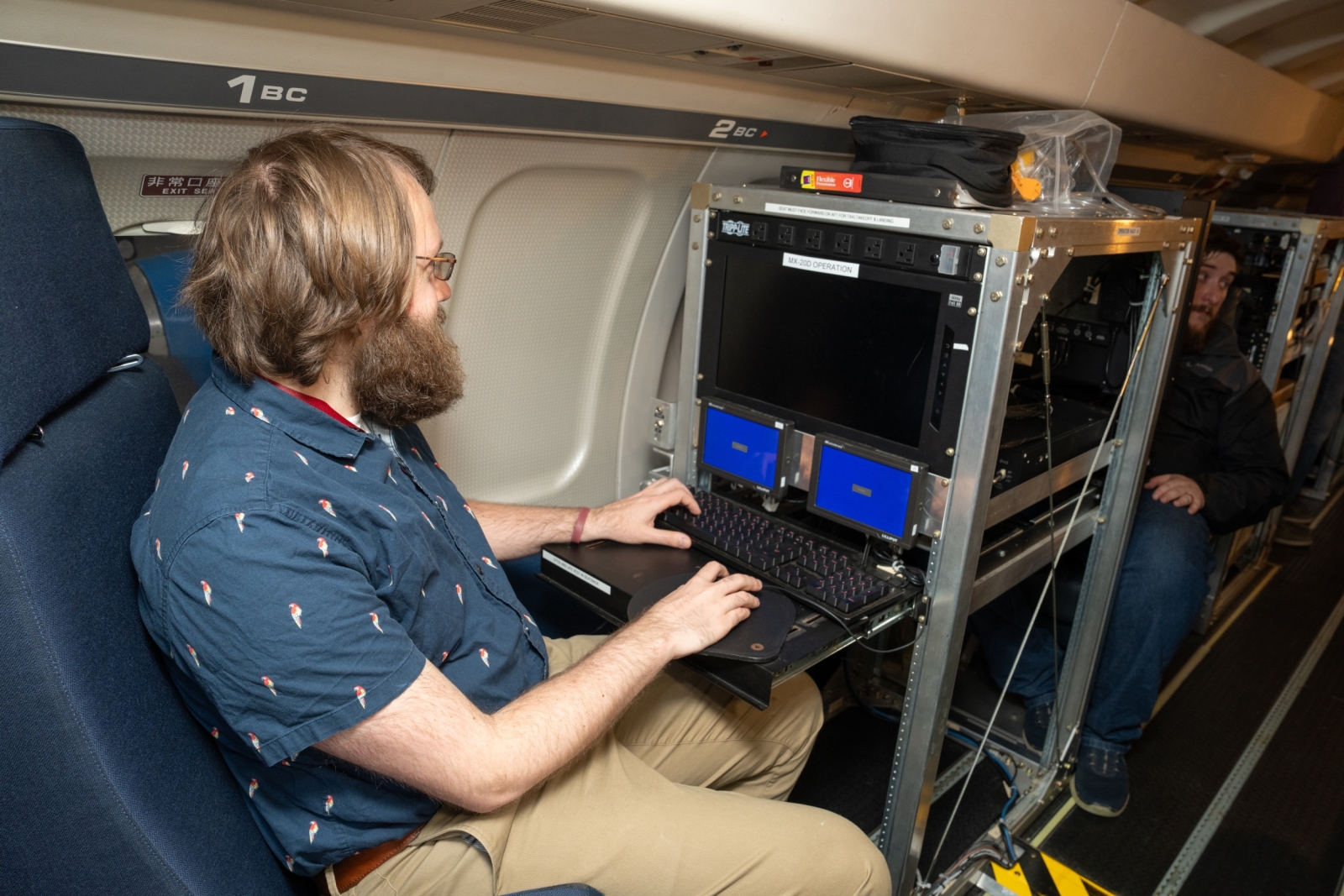 A researcher sits computer equipment inside of an airplane.