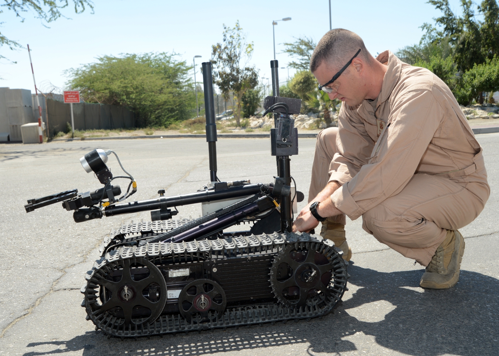 A U.S. Navy technician kneels down to adjust an explosive ordnance disposal (EOD) robot. 