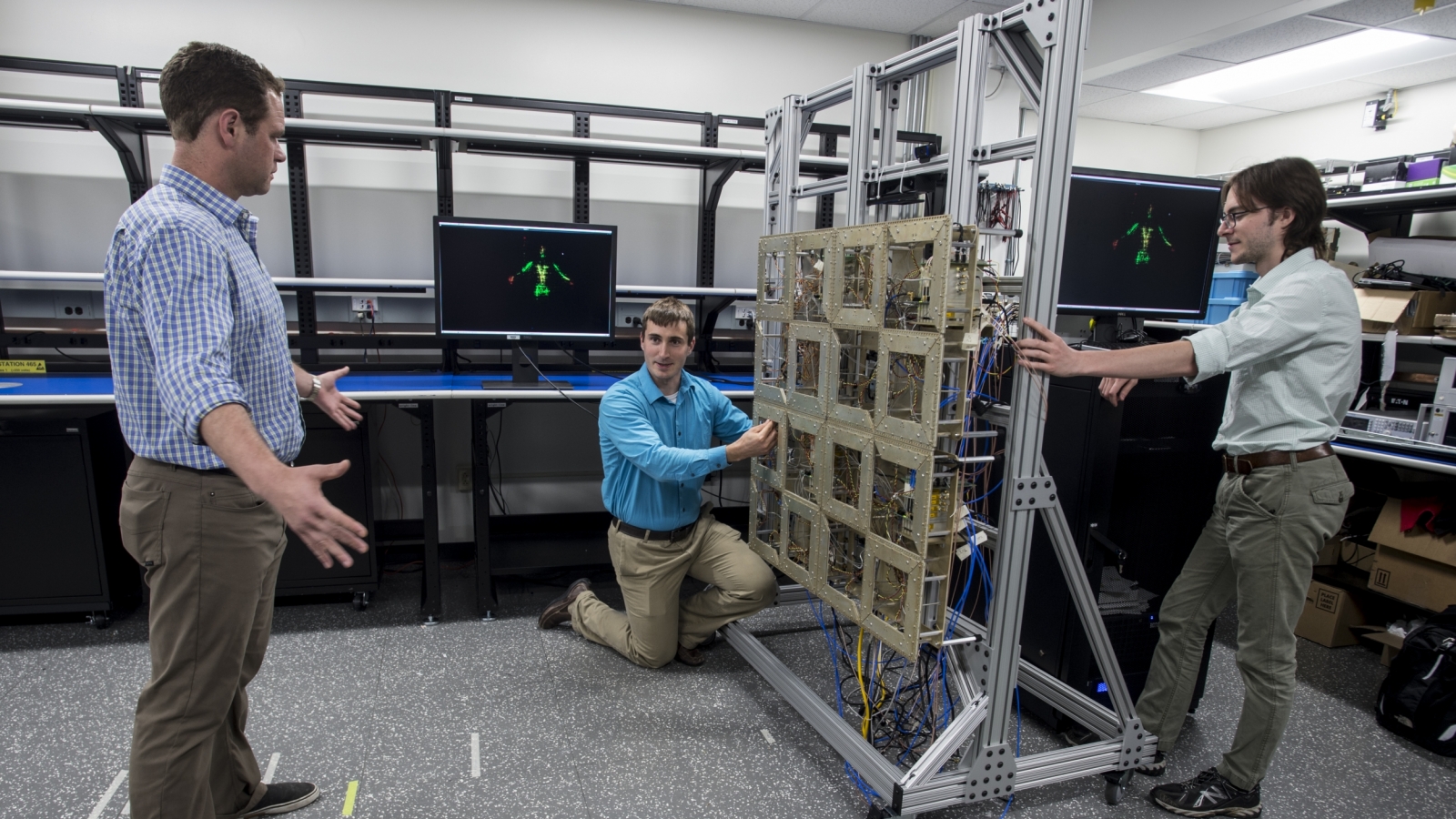 Researchers test the prototype standoff microwave imaging system. The antennas emit radio signals that reflect off the person standing in front of the array; the system processes the reflections to create the image on the monitors in the background.  
