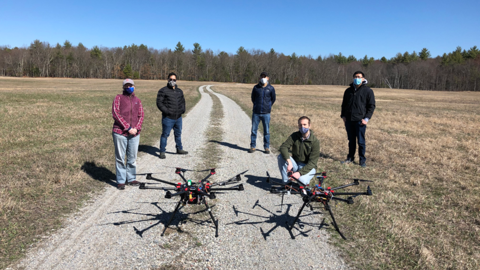 A group of five researchers pose in a field with two UAVs.