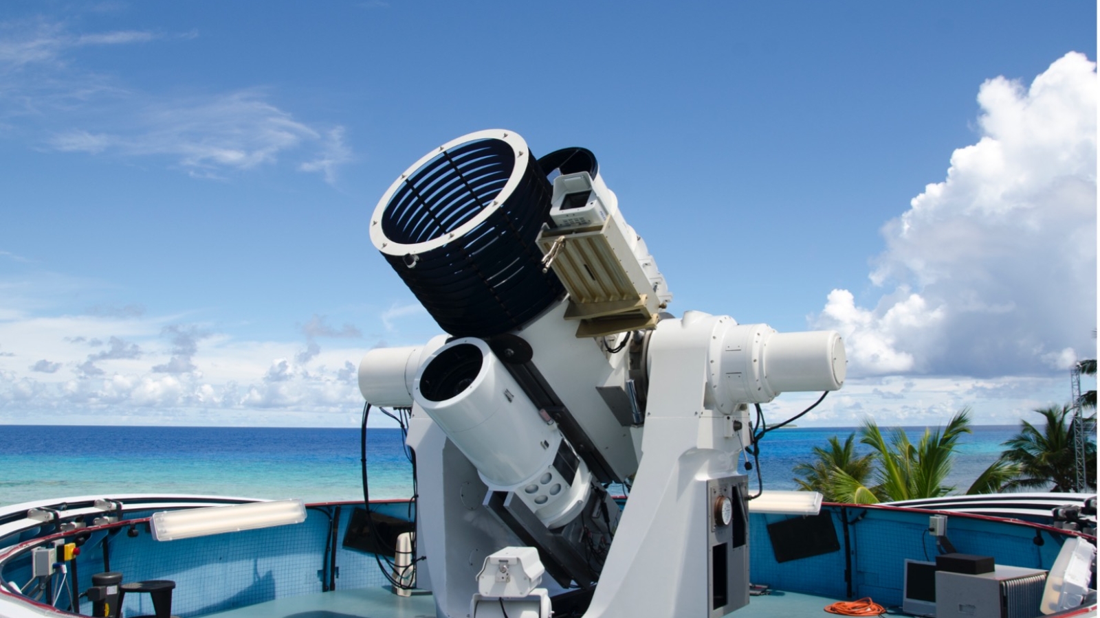 A photograph of a large optical system, with the ocean in the background. 