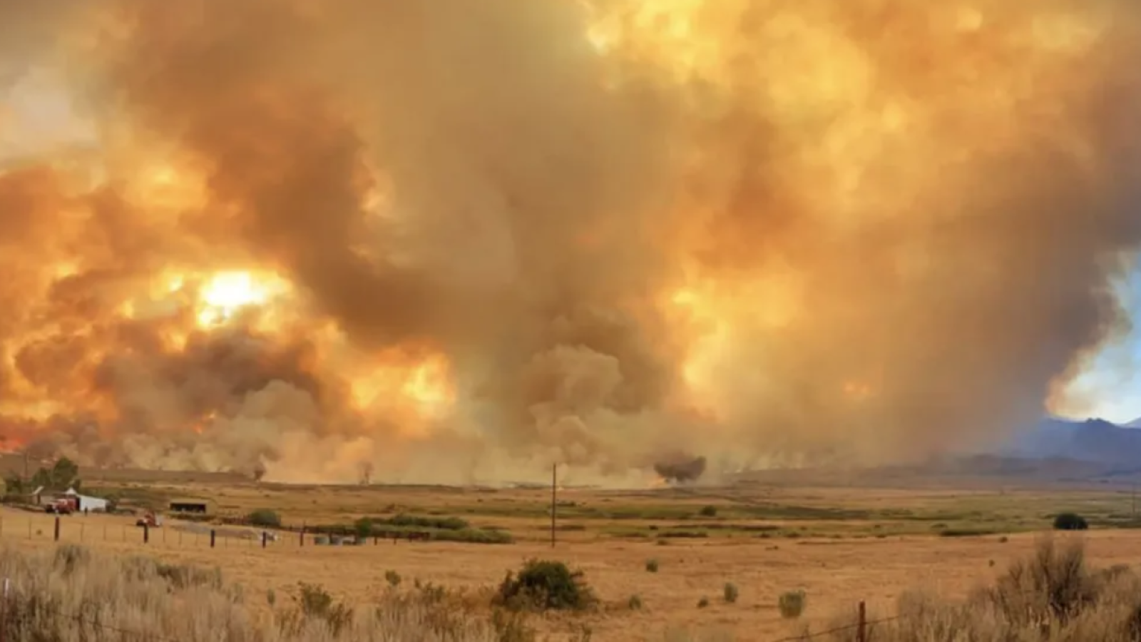 An image of the Slink wildfire showing flames and smoke rising over a field.