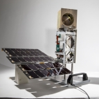 A small satelitte photographed against a white background. About , about 10 cm X 10 cm X 36 cm in size, it consists of a small solar panel array, connected to the satellite bus standing upright, topped with a golden cube. 