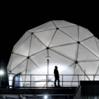 The 38-foot-wide radome protecting the Multi-Band Test Terminal — a large antenna on an MIT Lincoln Laboratory building rooftop — is shown illuminated at night. 