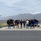 A team of eight stands in front of two sensor-equipped vehicles, with mountains in the backdrop. 