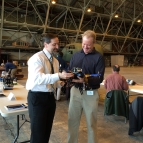 Two individuals hold and look at a drone at an Air Force Base indoor test range.