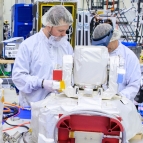 At Kennedy Space Center, Laboratory staff members Justin Dunbeck (left) and Steven Constantine unpack and examine the Optical Communications System payload for NASA's Artemis II mission to the Moon. Photo: NASA/Glenn Benson.