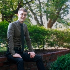 Connor Mathews sits outside on a brick wall 