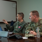 Colonel Joseph Monaco, left, and Lieutenant Colonel Tim Heaton sit at a table discussing a presentation they are being briefed on.