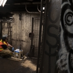 Laboratory staff member in orange vest is placing sampling equipment on the floor in a dark subway platform. 