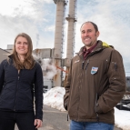 Jean Sack and Chris Lashway pose for a photo outside, with power-plant infrastructure in the background.