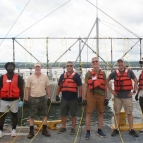 A group of researchers smile on a boat for a group photo. 