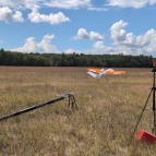 The research team's data collection drone is being launched from a ramp in a field on a clear day. 