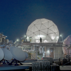 Four satellite dishes and two radomes, each covering satellite communications antennas, are shown on the roof of Lincoln Laboratory among other equipment.