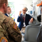 ARPA-H program manager Bon Ku faces the camera while talking to service members who are in the foreground. Part of the PSI vehicle's patient chair setup is visible next to Ku. 